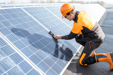 Wall Mural - well-equipped worker in protective orange clothing installing solar panels, measuring the angle of i