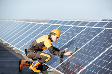 Wall Mural - well-equipped worker in protective orange clothing installing solar panels, measuring the angle of i