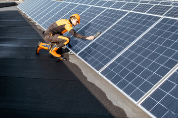 Wall Mural - well-equipped worker in protective orange clothing installing solar panels, measuring the angle of i