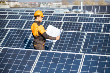 Wall Mural - Engineer in protective workwear with blueprints of solar station project on a photovoltaic rooftop plant. Concept of designing power plants