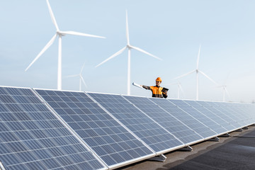 Wall Mural - view on the rooftop solar power plant with engineer in protective workwear and windturbines on the b