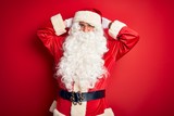 Fototapeta Na ścianę - Middle age handsome man wearing Santa costume standing over isolated red background relaxing and stretching, arms and hands behind head and neck smiling happy