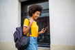 © mimagephotos - Side of young black woman walking with mobile phone and bag