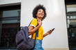 © mimagephotos - happy young black woman walking outside with cellphone and bag