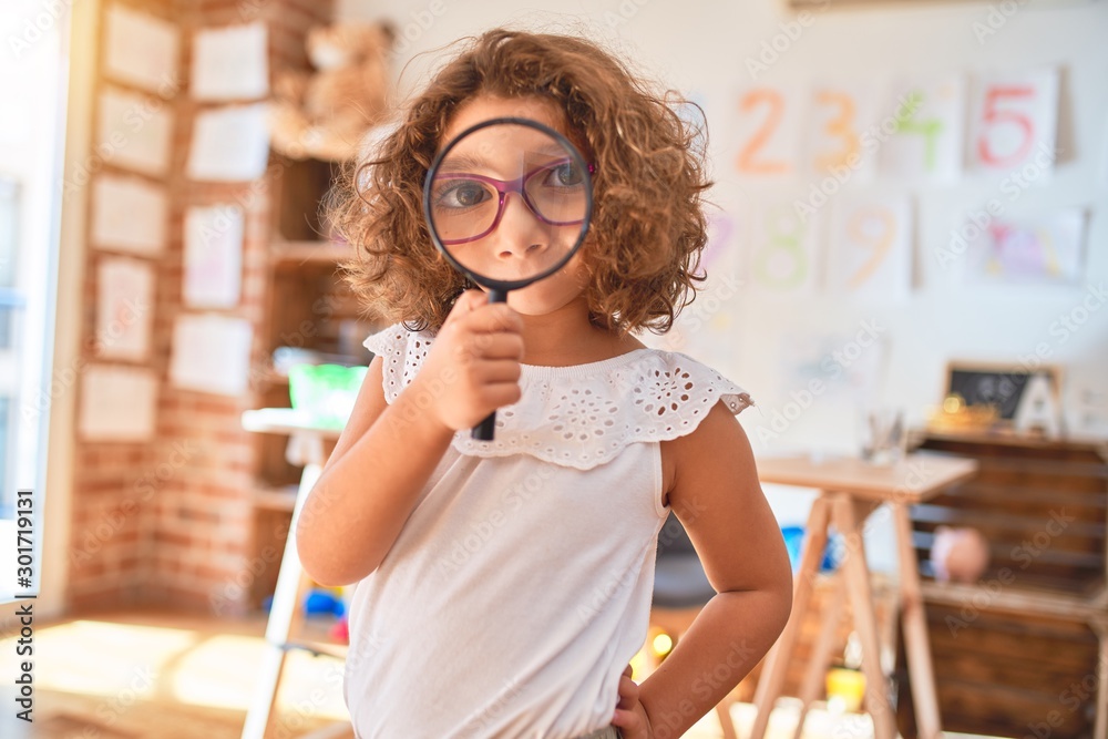 Beautiful toddler standing  wearing glasses using loupe at kindergarten - obrazy, fototapety, plakaty 