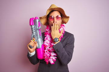 Canvas Print - Young businessman wearing water gun hawaiian lei hat glasses over isolated pink background cover mouth with hand shocked with shame for mistake, expression of fear, scared in silence, secret concept