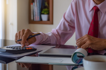 Wall Mural - Business man hand using calculator, writing and signing cheque book with laptop computer on the wooden table at modern home office.