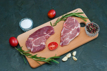 Wall Mural - Flat lay, pork, raw steaks and spices, garlic, salt, pepper, sliced tomatoes and rosemary on cutting board