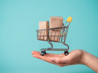 toy shopping cart with boxes in female hand over blue background. copy space for text or design. ssa