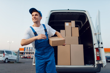 Deliveryman holds parcels at the car, delivering