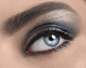 Beautiful woman eye close-up. Young Woman Blue one eye macro shoot. Holiday smoky eyes make-up, Macro Closeup eye looking up, closeup. Eyelashes, eyebrows, iris close-up