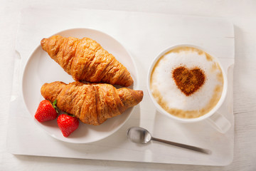 Wall Mural - Valentines day.  Cup of cappuccino coffee with drawn heart and fresh croissants, top view