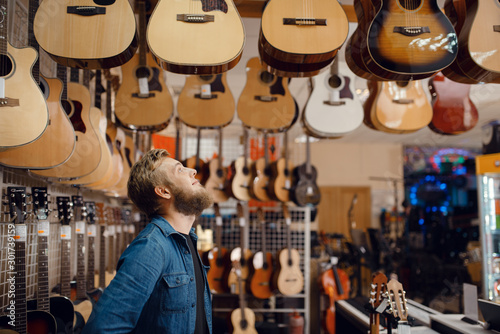 Fotografía Young guy choosing acoustic guitar in music store