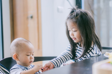 Wall Mural - Little sister sharing chocolate bar to her baby brother.Toddler kid meeting new sibling.Cute girl and baby boy relax at home in Japan.Family with children at home. Love, trust and tenderness.