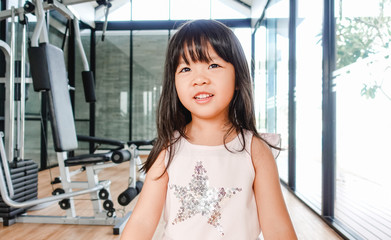 Wall Mural - Little asian girl working out with dumbbells at gym and tired face.