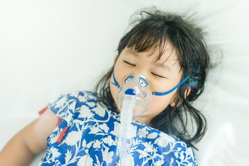 Sick little girl 4 years old inhale medication by inhalation mask to cure Respiratory Syncytial Virus (RSV) on hospital bed.Asian child girl inhales couples containing medication to stop coughing.