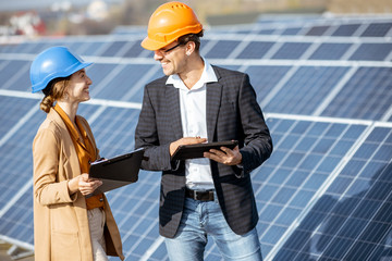 Wall Mural - Man and woman dressed in the suits and hard hat as an engineers or business people examining solar station with digital tablet