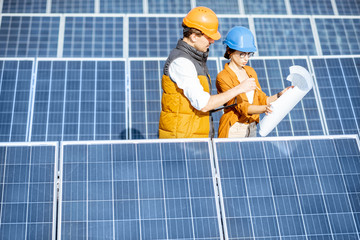 Wall Mural - two engineers or architects examining the construction of a solar power plant, standing with bluepri