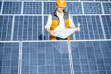 Wall Mural - Portrait of a handsome engineer in protective helmet standing with blueprints on a solar power plant. Solar station development concept