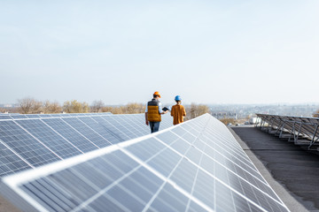 Wall Mural - view on the rooftop solar power plant with two engineers walking and examining photovoltaic panels. 