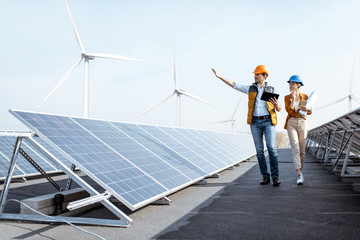 Wall Mural - view on the rooftop solar power plant with two engineers walking and examining photovoltaic panels. 