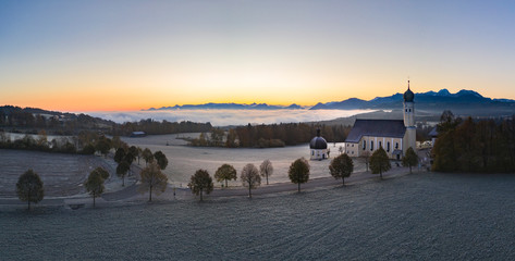 Wall Mural - beautiful foggy autumn morning in bavaria - aerial view of wilparting church before alps in chiemgau