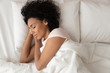 © fizkes - African American woman with hands under cheek sleeping in bed