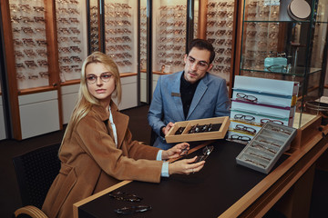 Sticker - Woman is choosing her new glasses at optical store with help of shop consultant.