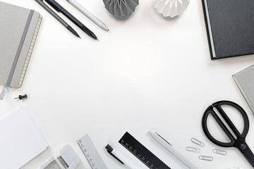 High angle flat lay desk with various black, gray and white stationery office working tools like scissors, pens, pencils and notebooks and empty copy space in middle