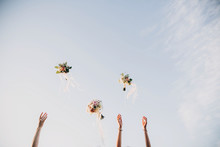 Bride And Bridesmaids Throwing Wedding Bouquets Up In The Sky In Evening Soft Light. Stylish Wedding Bouquets With Ribbons In Sky. Happy Moment