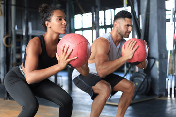 Beautiful young sports couple is working out with medicine ball in gym.