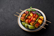 Paneer Tikka at skewers in black bowl at dark slate background. Paneer tikka is an indian cuisine dish with grilled paneer cheese with vegetables and spices. Indian food. Copy space