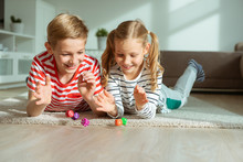 Portrait Of Two Cheerful Children Laying On The Floor And Playing With Colorful Dices