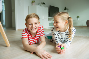 Wall Mural - Portrait of two cheerful children laying on the floor and playing with colorful dices