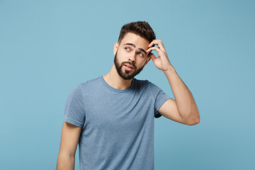 Wall Mural - Young pensive man in casual clothes posing isolated on blue wall background, studio portrait. People sincere emotions lifestyle concept. Mock up copy space. Putting hand on head, looking aside.