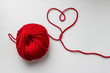 Ball of red yarn with a heart-shaped thread on white background