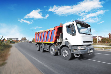 Wall Mural - Dump truck in motion on the countryside road against blue sky with clouds