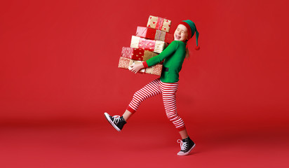 Wall Mural - cheerful funny child in Christmas elf costume with gifts on   red background.