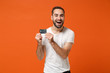 © ViDi Studio - Cheerful young man in casual white t-shirt posing isolated on bright orange wall background studio portrait. People sincere emotions lifestyle concept. Mock up copy space. Holding credit bank card.
