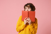Young Brunette Woman Girl In Yellow Sweater Posing Isolated On Pink Wall Background Studio Portrait. People Sincere Emotions Lifestyle Concept. Mock Up Copy Space. Holding Covering Mouth With Book.
