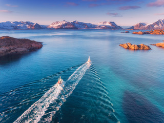 Wall Mural - aerial view of fishing boats, rocks in the blue sea, snowy mountains and colorful sky with clouds at