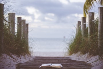 Closeup shot of an open bible on a wooden pathway towards the beach with a blurred background