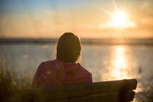 Female Sitting On A Bench Shot From Behind With A Blurred Sea In The Background