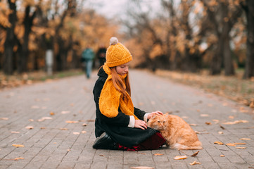 Sad and lonely freckles girl petting her pet - adorable red cat in the autumn trees valley.