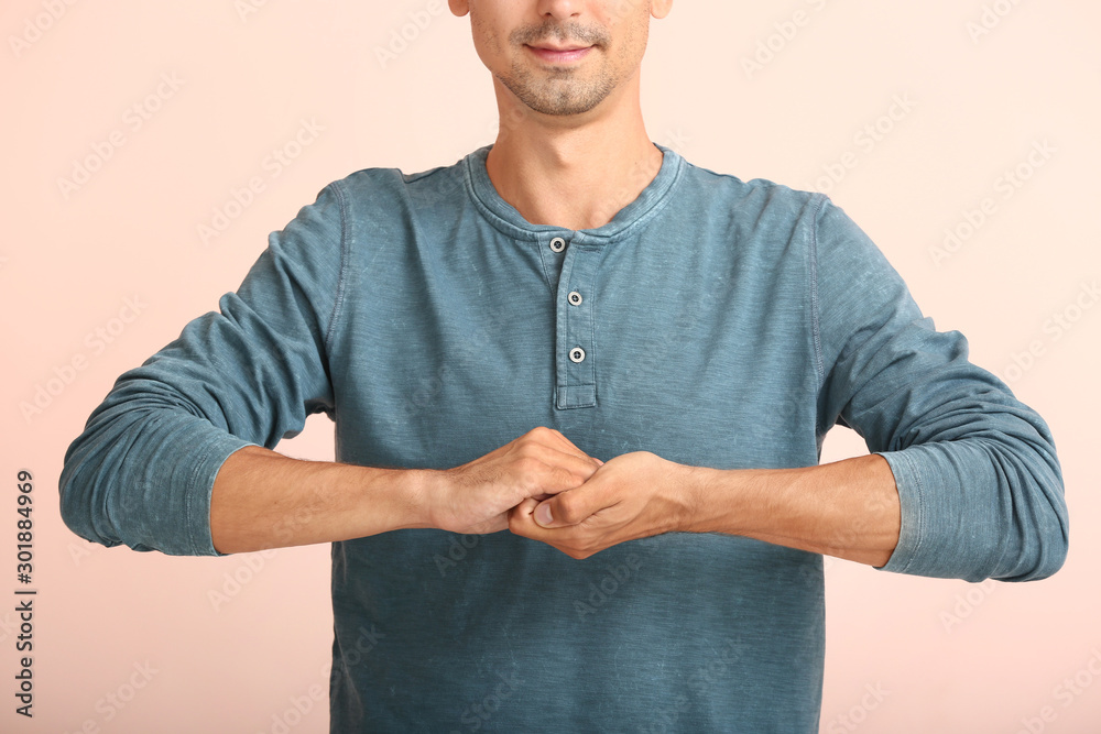 Young deaf mute man using sign language on color background