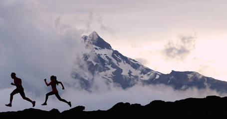 Running fit athletes people trail running with mountain summit background. Man and woman silhouetteon run training outdoors active fit lifestyle.