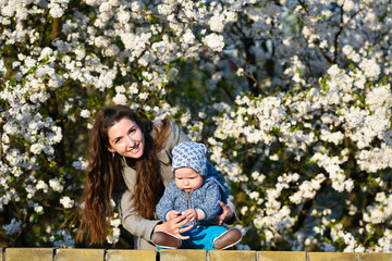 Toddler with mom on the background of flowering trees. little baby on hands of mother. woman playing with child outside in blooming spring garden. portrait of family of two people. happy family concep