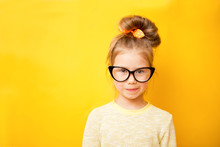 Portrait Of Child Girl In Glasses On A Yellow Background. Copy Space