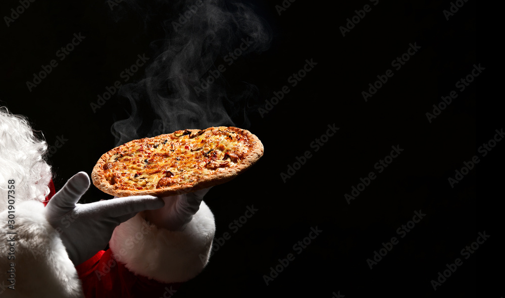 Happy Santa Claus hold big hot steaming pizza offering with copy space. New year and Xmas fast food - obrazy, fototapety, plakaty 