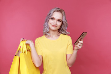 Beautiful female person with phone and shopping bags standing at the pink wall